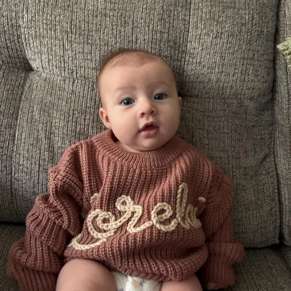 Baby in a rust sweater with cream embroidered lettering