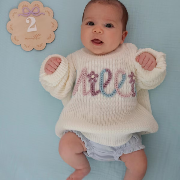 Baby in a cream sweater with a colorful embroidered name